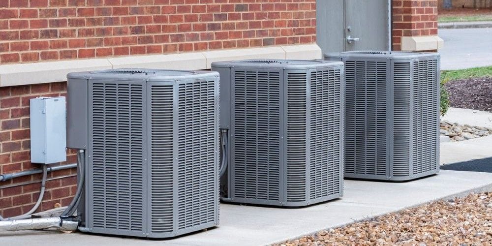Air conditioners on a cement foundation outside of a brick building.