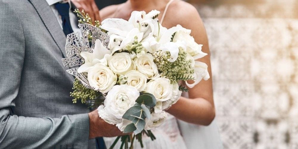 A bride holding bouquet of flowers standing next to her groom.