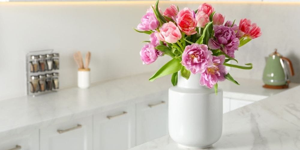Beautiful bouquet of colorful tulip flowers on white marble table in kitchen.