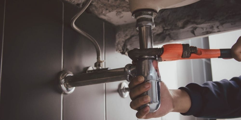 Plumber fixing a leaky pipe under the bathroom sink.